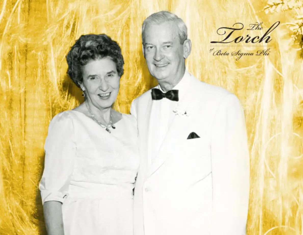 Black and white photo of a smiling couple in formal attire with a gold background.