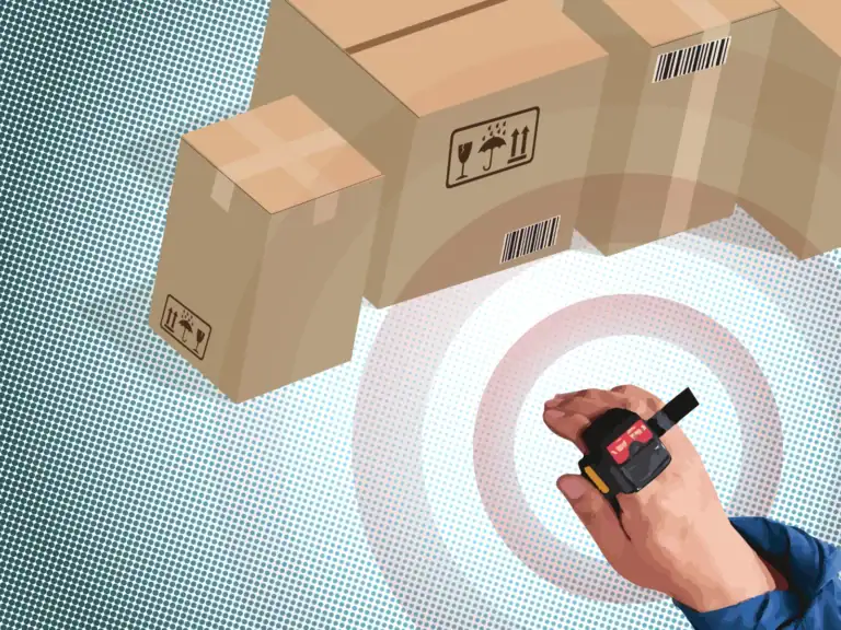 Hand holding a barcode scanner over cardboard boxes in a warehouse setting.