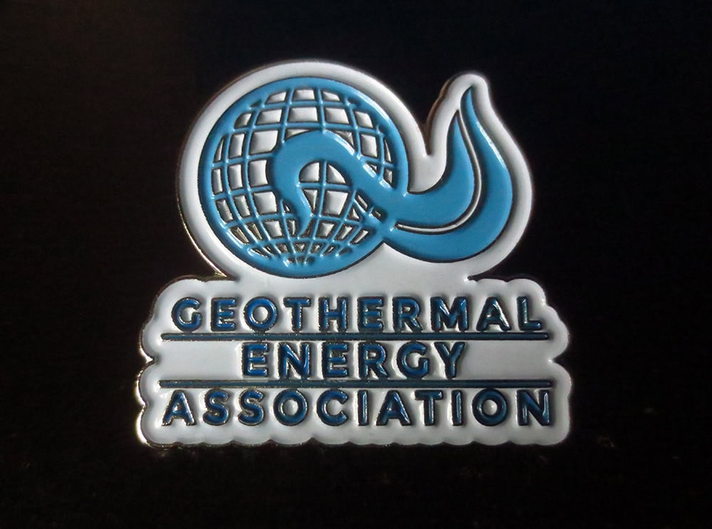 Globe with wave symbol and text emphasizing geothermal energy association, styled as a metal badge.